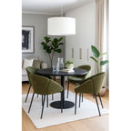 Sillón de chenilla verde en un salón con plantas y luz natural